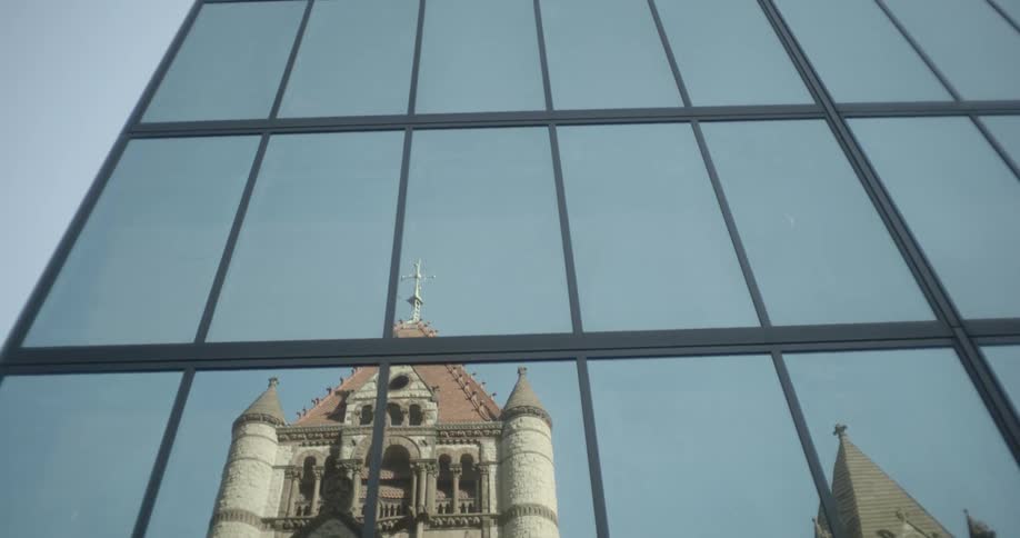 A reflection of the historic Trinity Church in Boston is seen in a modern glass skyscraper, with the camera tilting up to the sky