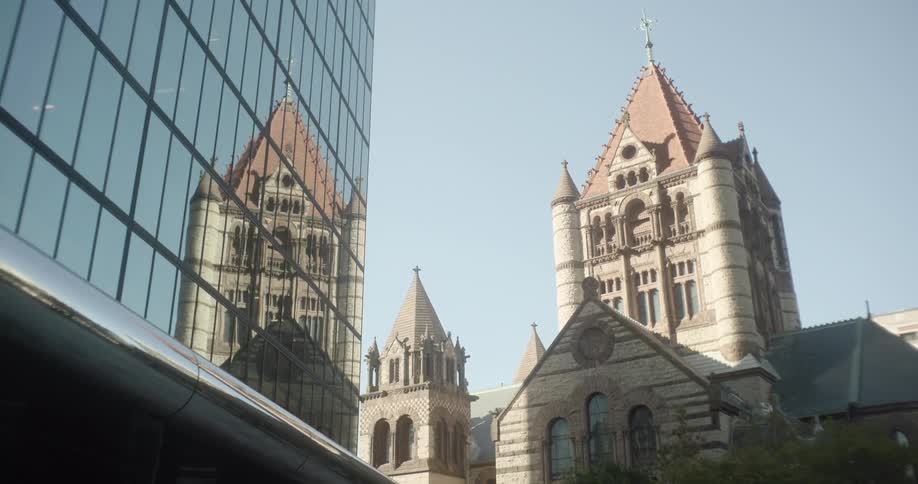 The historic Trinity Church in Boston is reflected in the glass facade of a modern skyscraper, showcasing a contrast of architectural styles