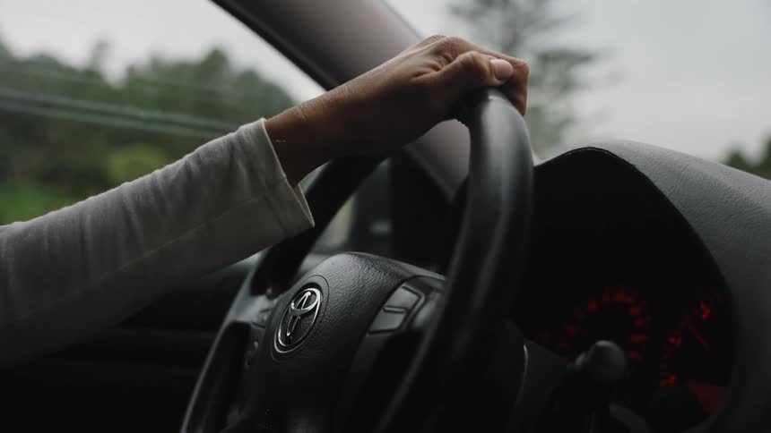 A close-up shot of a person's hand gripping the steering wheel while driving on an overcast day