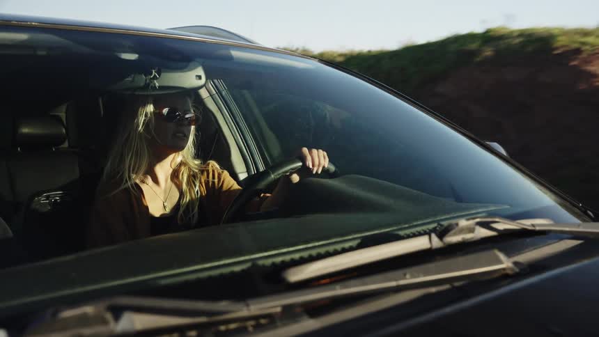 Slow motion shot of a stylish young blonde woman driving her car on an adventurous road trip through the countryside