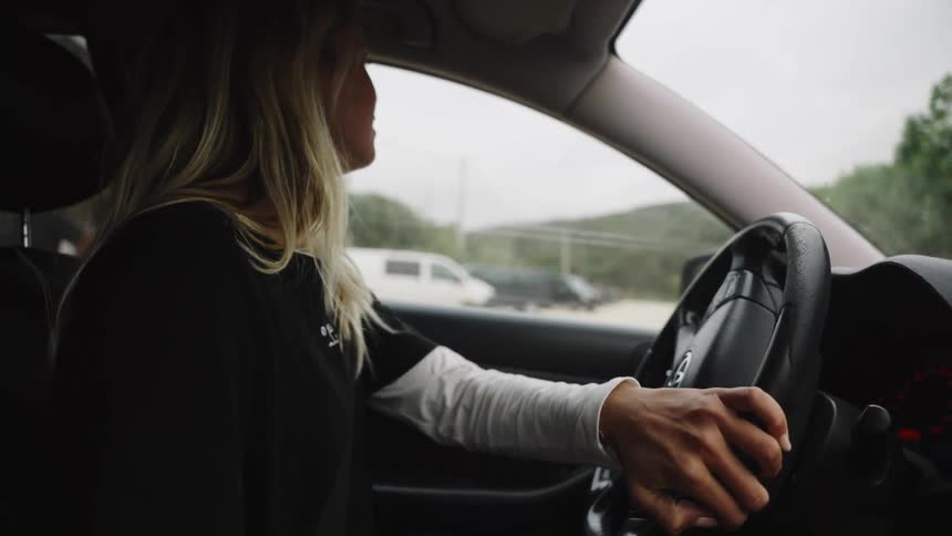 Interior slow-motion shot of a blonde woman driving her car and tapping her fingers on the steering wheel