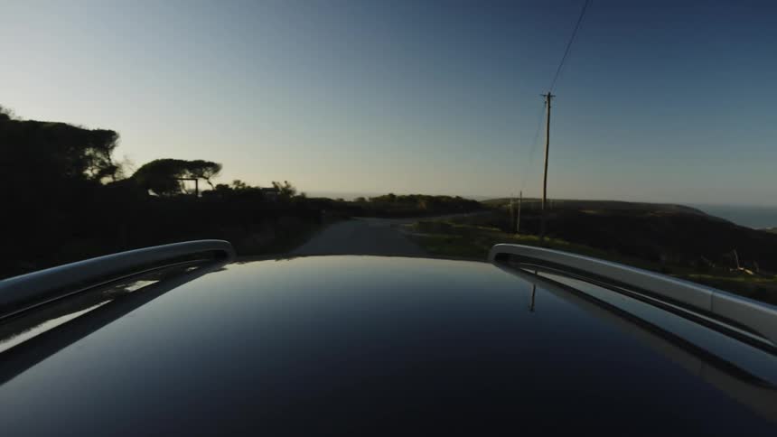 A car drives along a scenic coastal highway with ocean views during a beautiful golden hour sunset