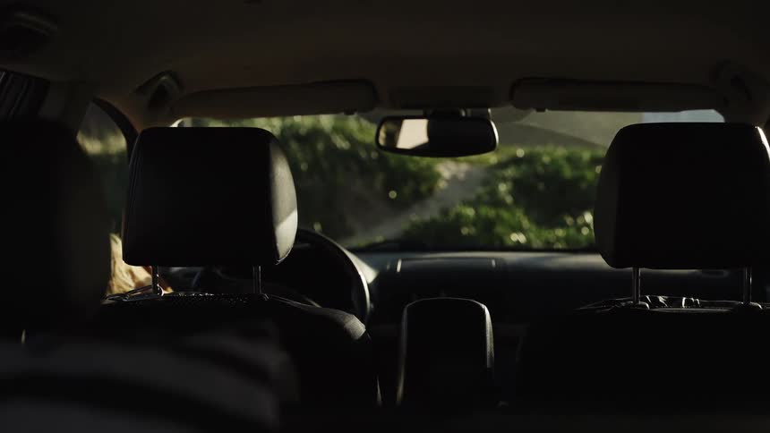 Over the shoulder shot from the backseat of a woman driving a car during golden hour