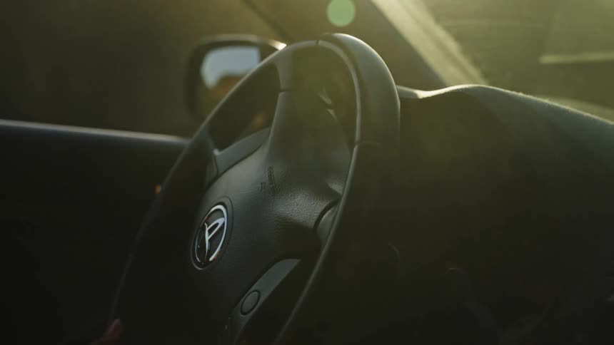 A cinematic slow-motion shot from inside a car driving along a winding coastal highway during a beautiful golden hour sunset