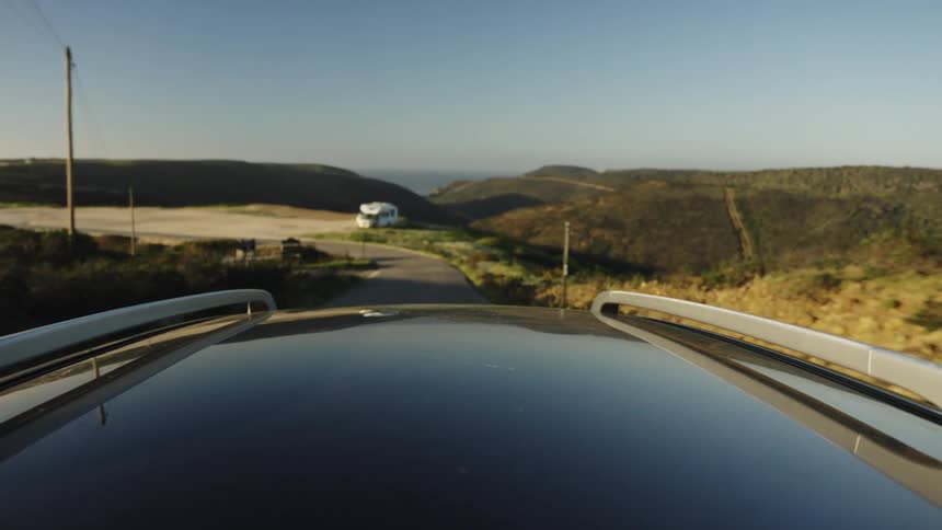 Slow-motion point-of-view from a car roof driving down a scenic rural road towards the coast