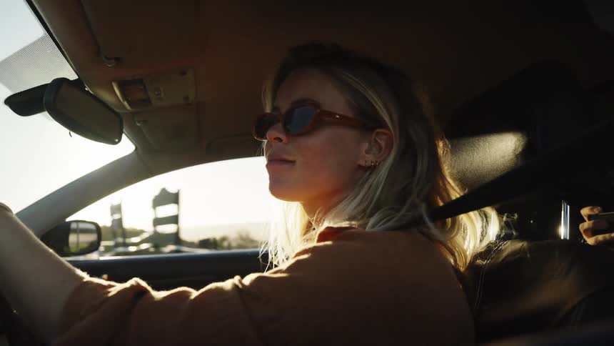 Slow motion shot of a stylish young woman driving her car during a scenic road trip at sunset