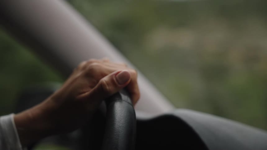 A close-up of a woman's manicured hand holding the steering wheel while driving down a road