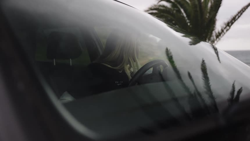 A young woman takes a moment in her car by the sea before unbuckling her seatbelt and stepping out to enjoy the coastal scenery