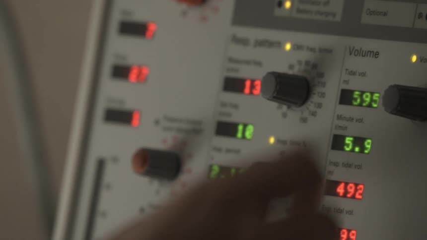 Close-up of a medical professional's hand adjusting the knobs and settings on a life support ventilator machine