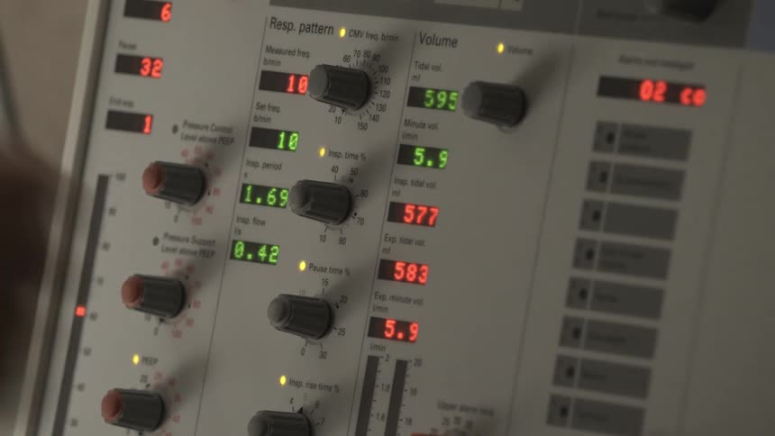 A medical professional adjusts the settings on a ventilator machine in a hospital, with blinking lights and changing numbers on the digital display