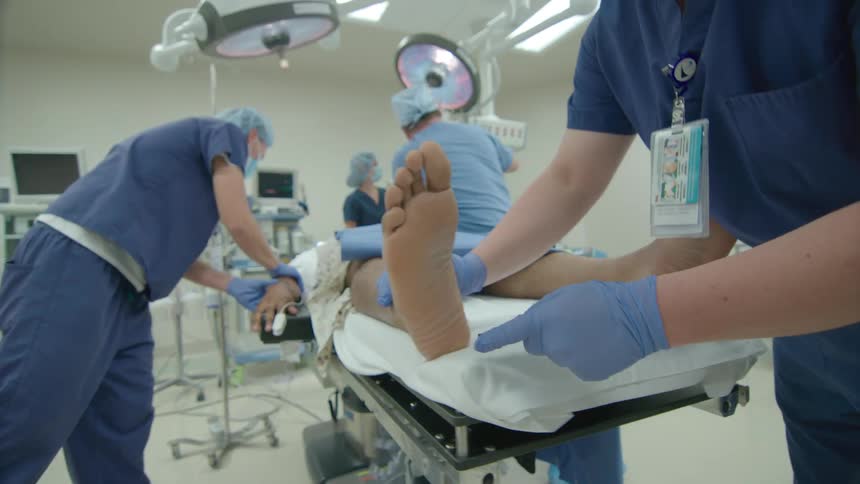 Slow pull back shot reveals a team of surgeons and nurses preparing a patient for an operation in a modern hospital