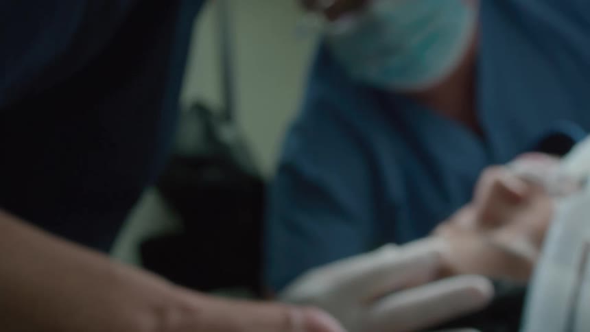 Out-of-focus close up shot of a patient lying down with an oxygen mask on while a medical team operates