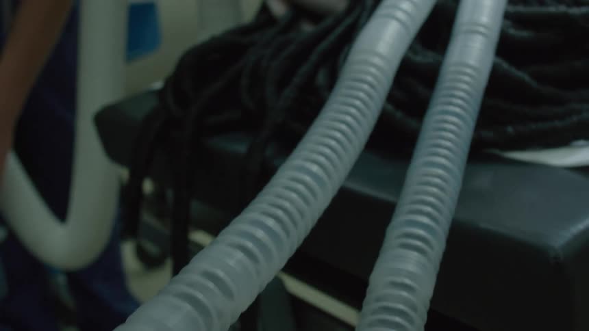 A close-up of a ventilator tube slowly reveals an unconscious patient on an operating table as medical staff works in the background