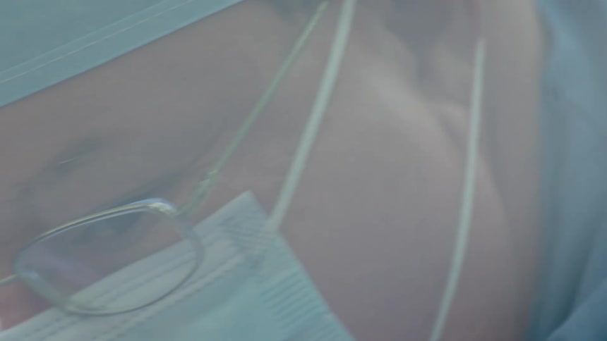 Extreme close-up panning shot reveals a focused surgeon wearing a mask and glasses in the operating room