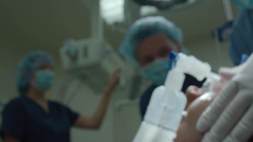 A blurry, first-person patient's point-of-view looking up at a team of surgeons in a hospital operating room