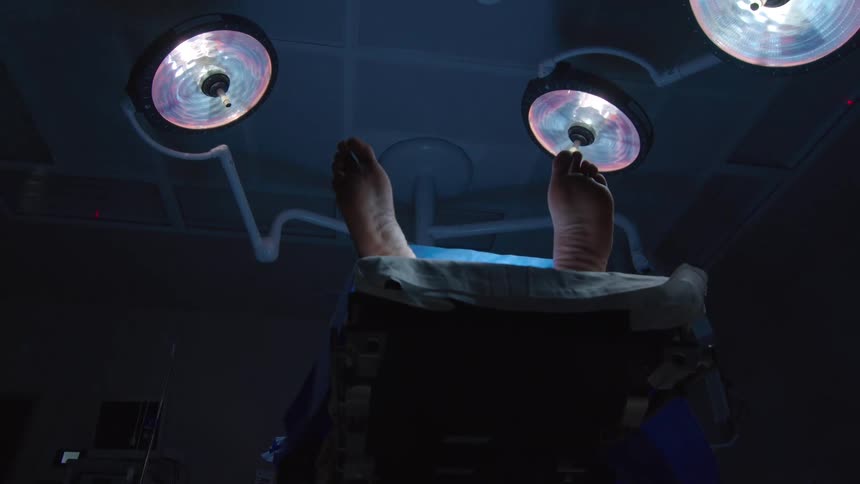 Low angle shot of a patient's feet on an operating table under surgical lights in a dark room
