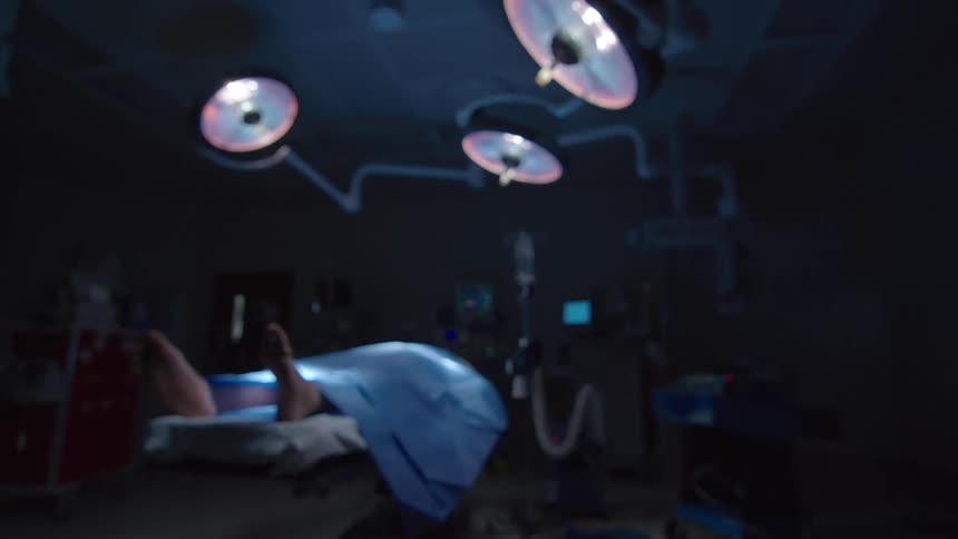 A dramatic, out-of-focus shot slowly comes into focus on a patient's feet on an operating table in a dark surgical theater