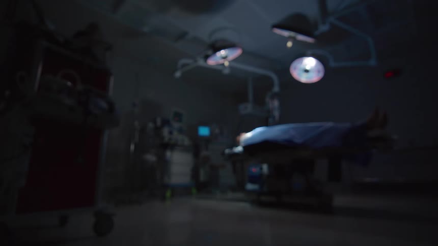 A slow rack focus reveals a patient lying on a table in a dark and empty operating room