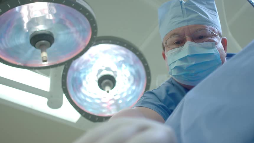 Patient's point of view looking up at a surgeon in an operating room with a focus pull from a pulse oximeter on their finger