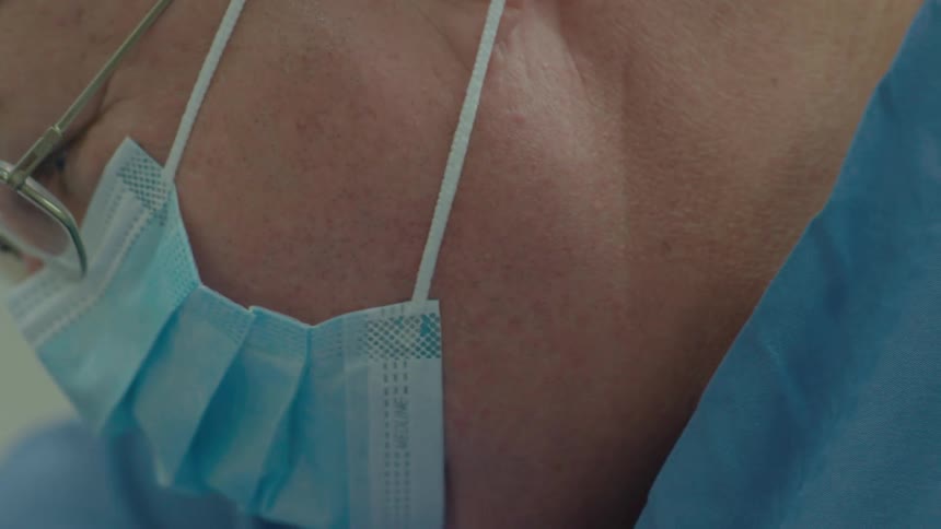 An extreme close-up slow-motion shot captures the intense focus of a surgeon in the middle of an operation