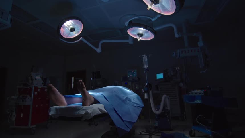 Dramatic wide shot of a patient lying still on an operating table in a dark hospital room