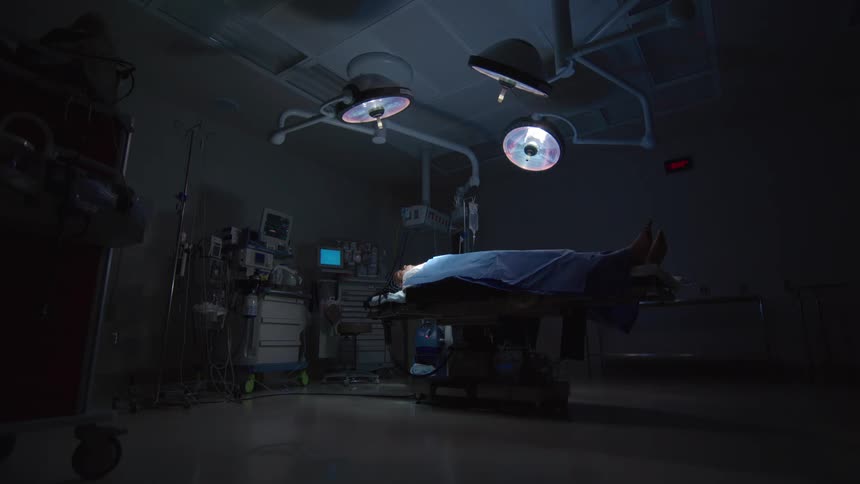 A patient lies on an operating table in a dark, empty hospital surgery room before a procedure
