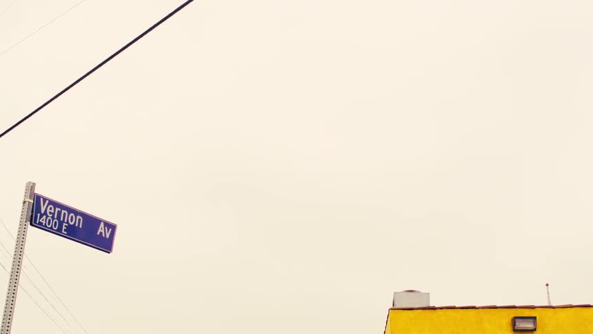 A slow pan from a Vernon Avenue street sign to a Compton street sign on an urban corner under an overcast sky