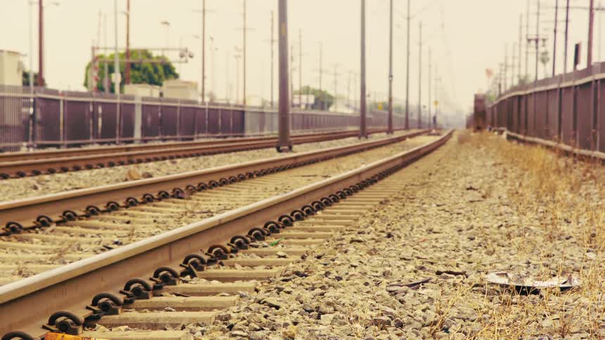 A low angle, static shot shows empty train tracks stretching into the hazy distance on a hot day