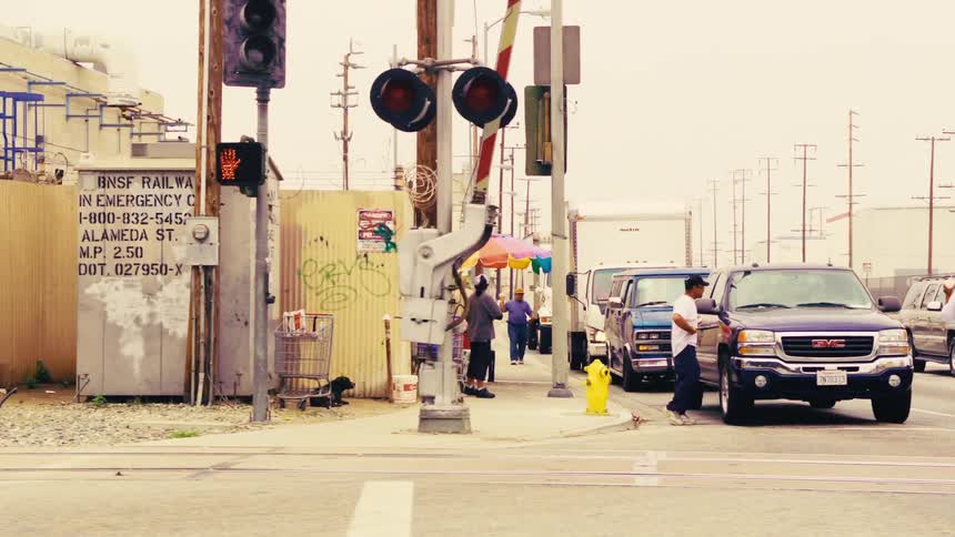 A slow-motion tracking shot reveals a graffiti-covered wall and a bustling street scene in an industrial urban neighborhood