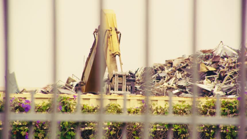 A yellow excavator with a large claw sorts through a massive pile of scrap metal in an industrial junkyard