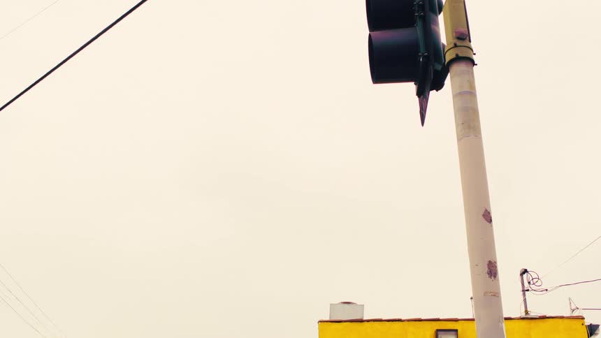 Low-angle slow pan of an urban street corner with a traffic light and yellow building against a white sky