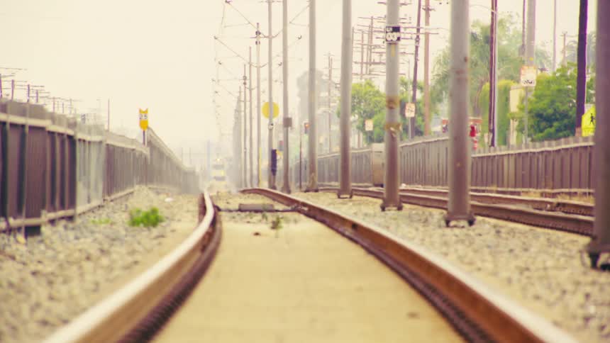 From a low angle, a yellow train travels down the tracks and passes by on an overcast day