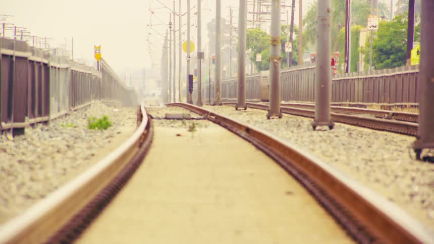A dreamy, low-angle shot of urban train tracks with a slow rack focus revealing an approaching train in the distance