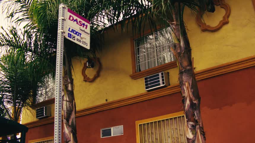 A slow pan reveals a colorful vintage-style motel, a bus stop, and a street corner in a Los Angeles neighborhood