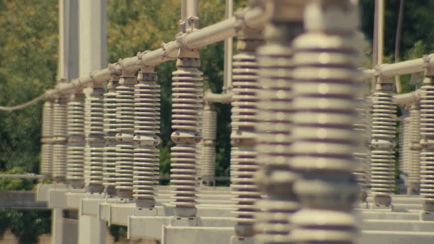 A slow tilting and panning close-up shot of ceramic insulators and conductors at a high voltage electrical power substation