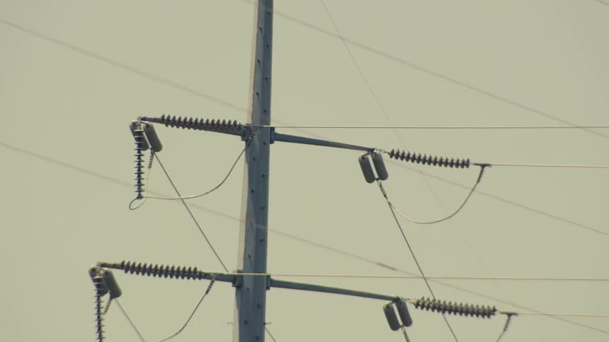 A slow reveal of a high-voltage electrical tower shows power lines shimmering in the heat against a hazy sky