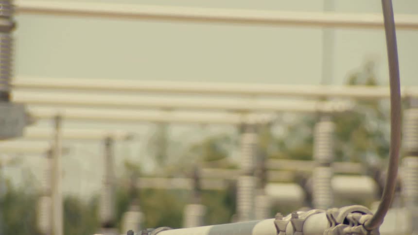 A slow pan and rack focus reveals a close-up detail of an electrical substation's conductor clamp