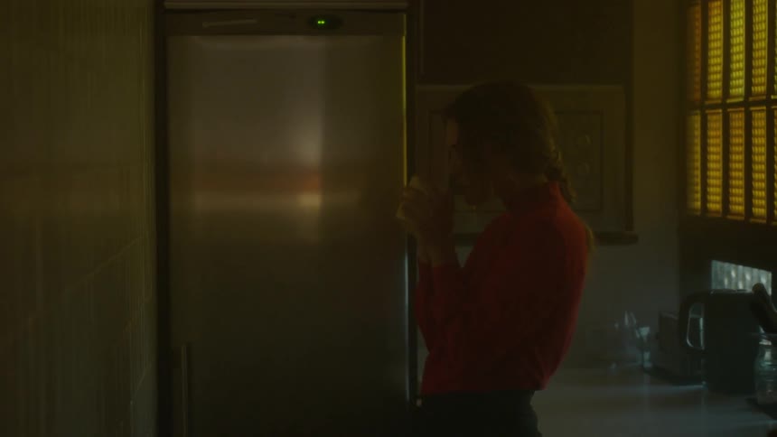 A woman takes a cup out of a kitchen microwave and drinks from it