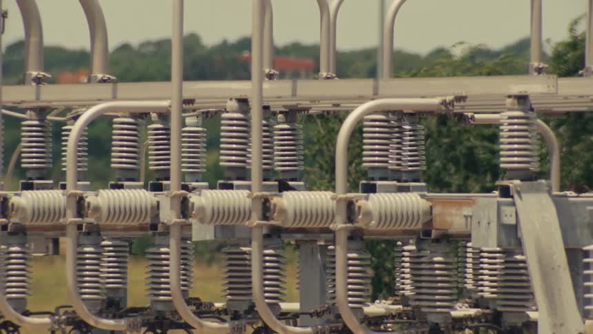 A detailed tilt and pan across the transformers and insulators of an electrical power substation on a hot day