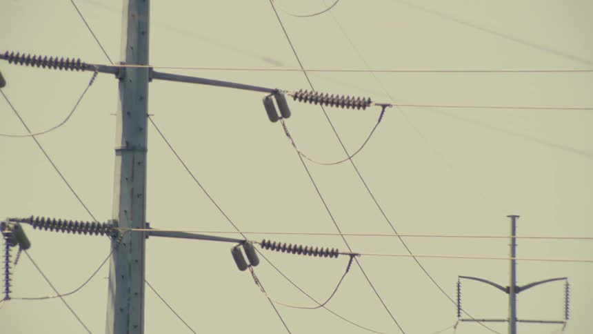 A slow tilt up of a high-voltage transmission tower and power lines against an overcast sky