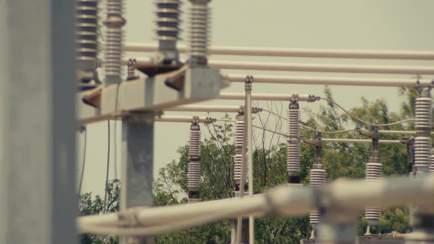 A close-up vertical tilt of the insulators and conductors at a large electrical power grid substation