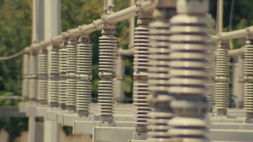 A close-up rack focus shot of ceramic electrical insulators at a high voltage power substation