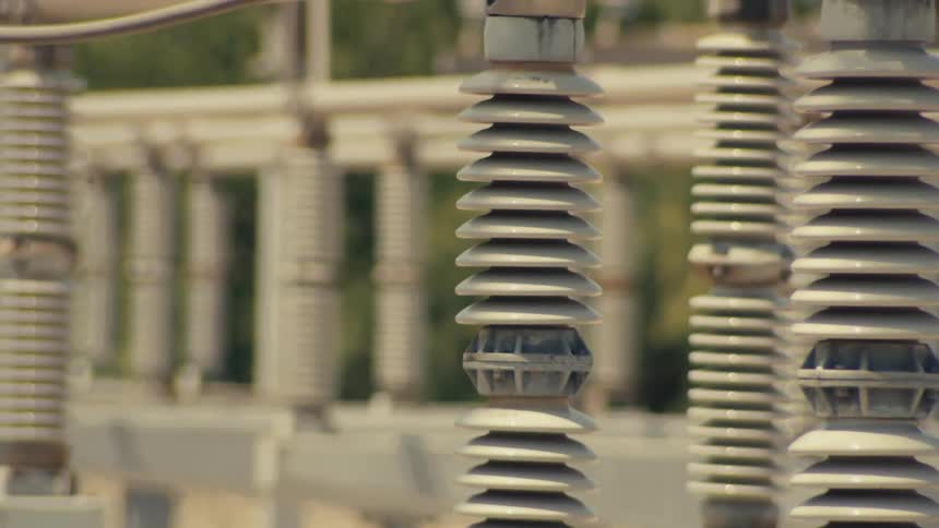A slow upward tilt reveals rows of ceramic insulators and metal structures at an electrical power substation