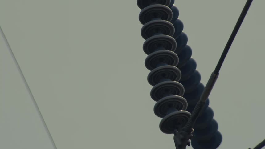 A close-up camera pan down a high-voltage power line, revealing the intricate details of its ceramic insulators and cables