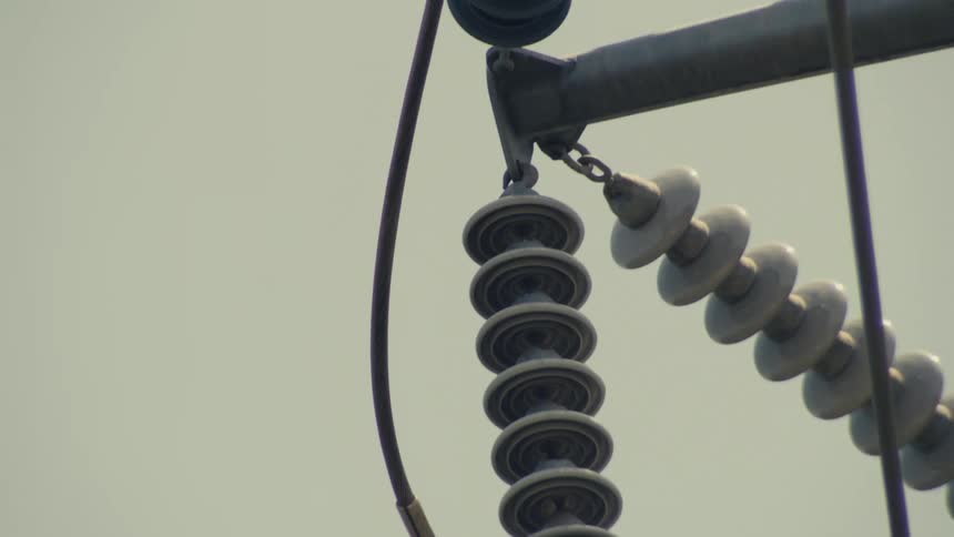 Close-up slow tilt down a section of a high-voltage power line revealing the intricate insulators and cables