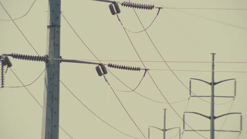 A slow zoom out reveals rows of industrial high-voltage power lines on a hot, hazy day
