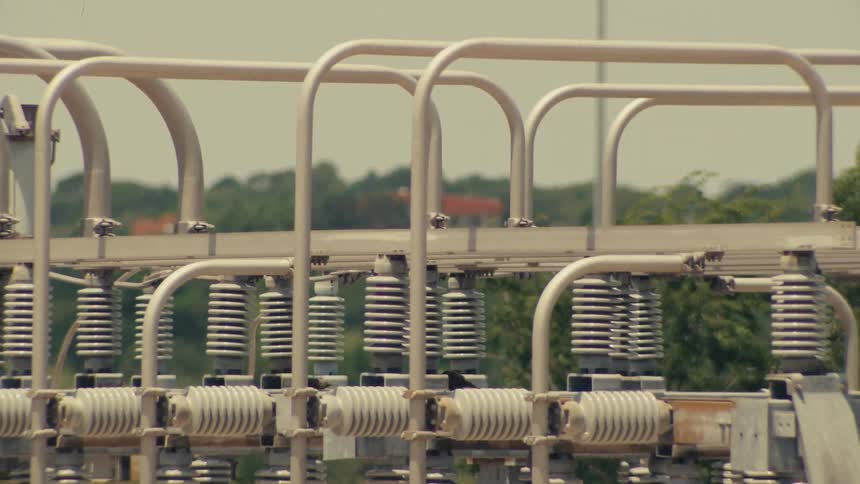 A detailed pan and tilt shot reveals the complex machinery of a high-voltage electrical substation on a sunny day