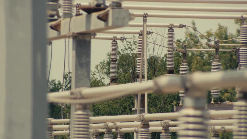 A detailed close-up shot slowly tilts down over the ceramic insulators of a high-voltage electrical substation
