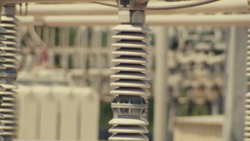 A close-up, slow tilt-up reveals a ceramic electrical insulator at a power substation
