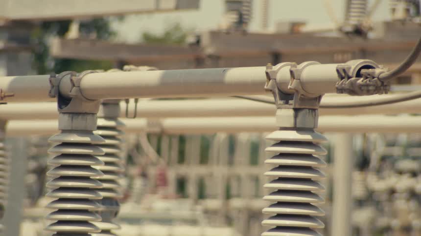 A slow pan across the intricate network of high-voltage insulators and transformers at an electrical power substation